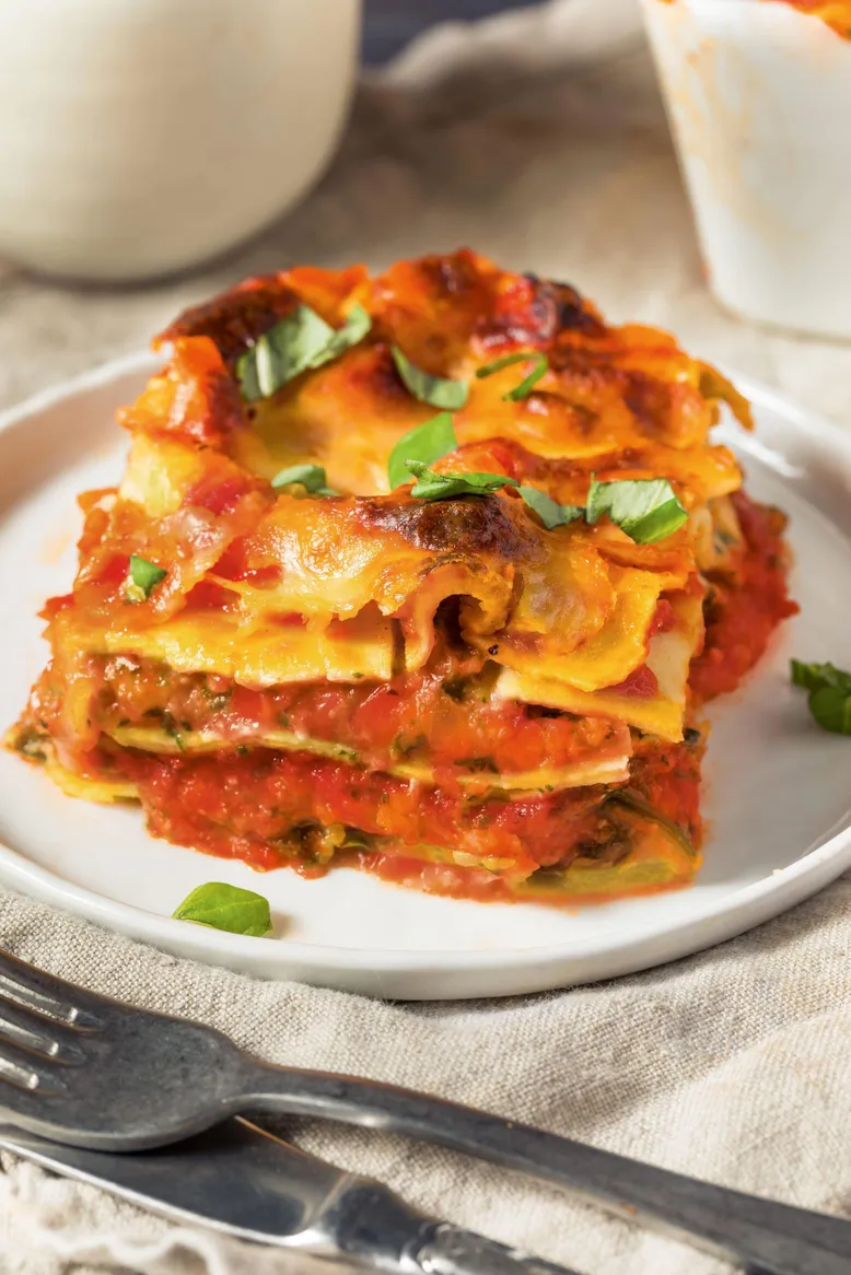 Part de lasagnes aux légumes et sauce tomate, basilic frais, sur une assiette blanche.