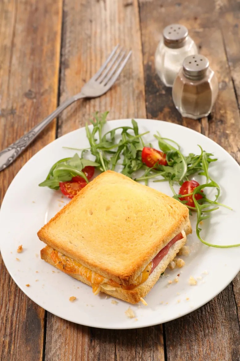 Croque-monsieur grillé accompagné d'une salade verte sur une assiette blanche.