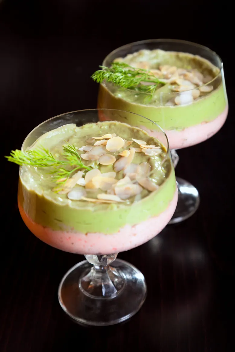 Deux verres de verrines d'avocat et mousse de crevettes, décorées d'aneth et d'amandes effilées.