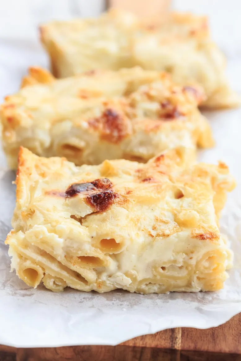 Trois tranches de gratin de macaronis au fromage, dorées et croustillantes, sur papier cuisson.