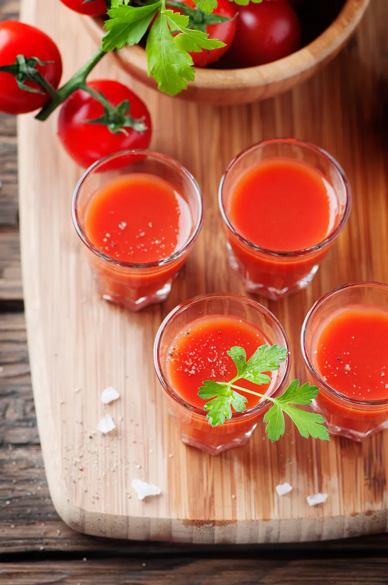 Quatre shooters de jus de tomate, garnis de persil, avec des tomates cerises.