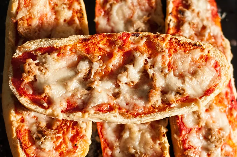 Gros plan sur des mini-pizzas au thon, sauce tomate et fromage fondu sur des baguettes.