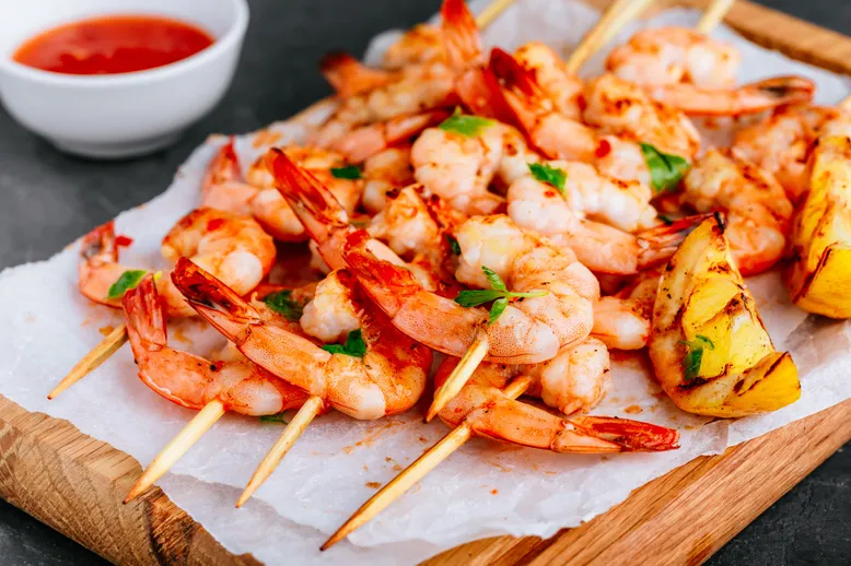 Brochettes de crevettes grillées avec quartiers de citron et sauce piquante.