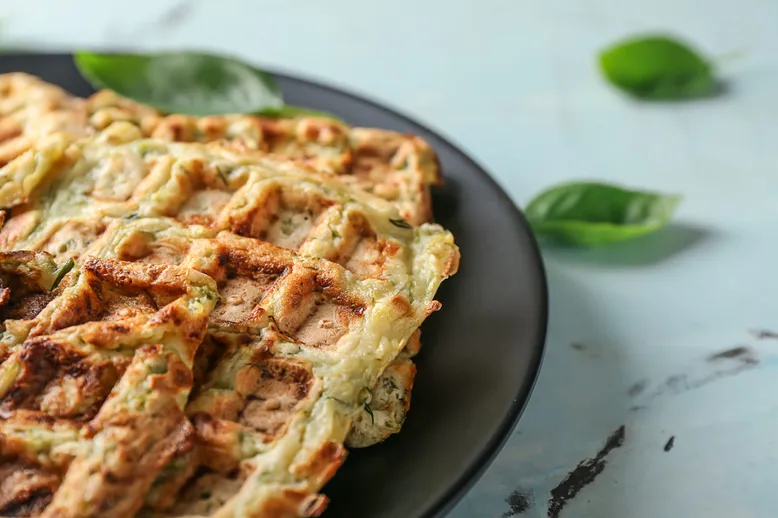 Gaufres salées aux courgettes et herbes, servies sur une assiette noire.