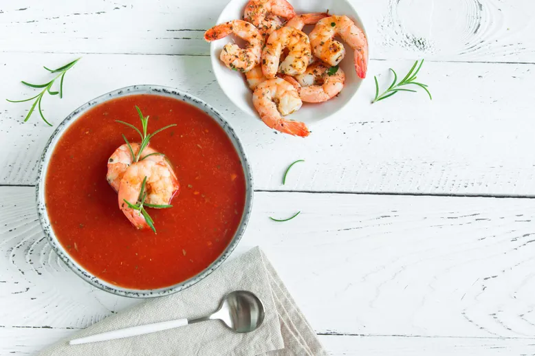 Bol de soupe de tomate aux crevettes et romarin, avec une cuillère et une serviette.