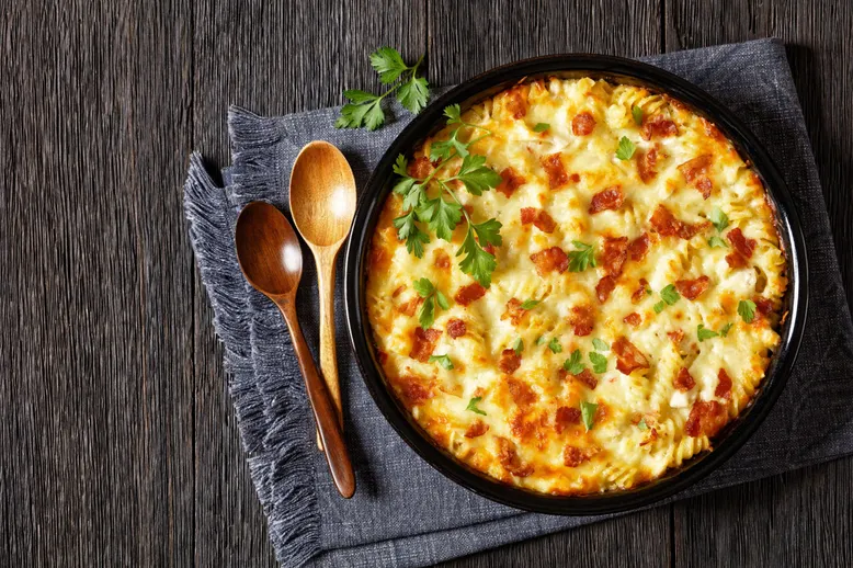 Plat de fusilli gratinés au fromage et thon, avec des cuillères en bois sur une table sombre.