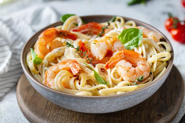 Bol de tagliatelles aux crevettes dans une sauce crémeuse, garni de basilic et de thym.