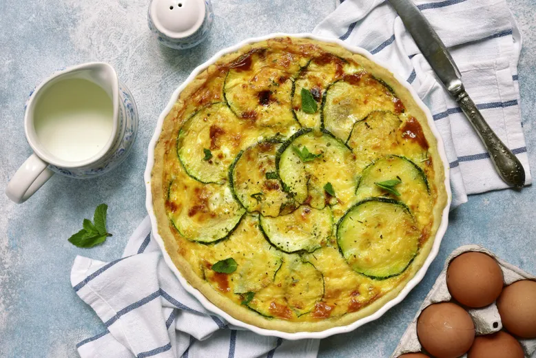 Quiche aux courgettes et fromage gratiné, garnie de feuilles de menthe.