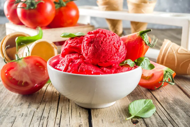 Bol de sorbet rouge (tomate) garni de basilic et quartiers de tomate, avec cornets de glace.