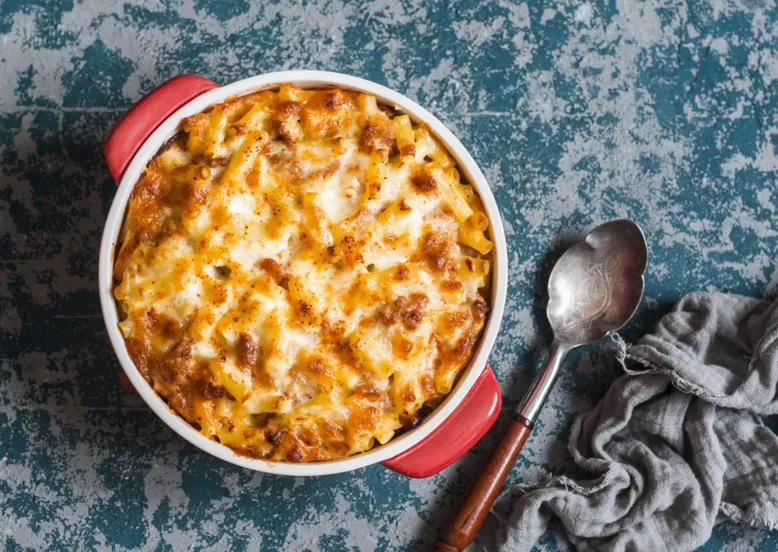 Plat rond rouge de gratin de macaronis avec une croûte de fromage dorée et une cuillère.