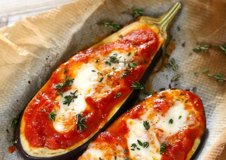 Deux moitiés d'aubergines rôties garnies de sauce tomate, fromage fondu et thym.