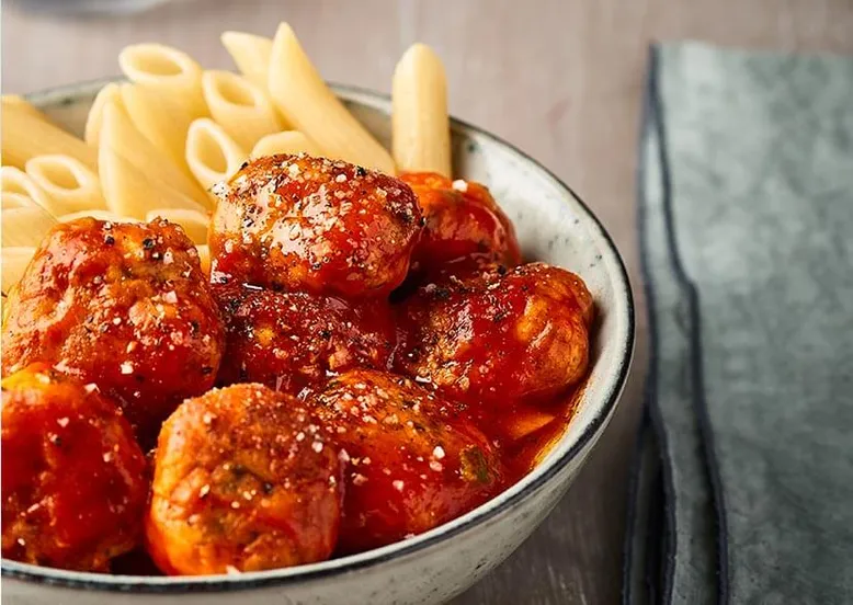 Bol de penne aux boulettes de viande en sauce tomate, parsemé de parmesan râpé.