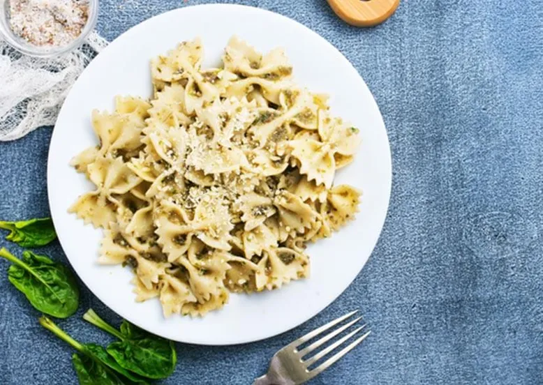 Assiette de farfalle au pesto et parmesan râpé, avec feuilles d'épinards frais.