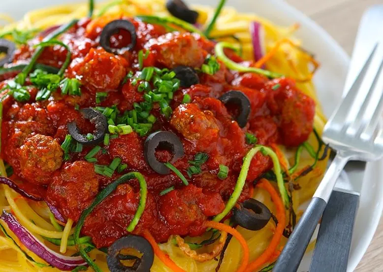 Assiette de spaghetti aux boulettes de viande, sauce tomate, courgettes en julienne et olives noires.