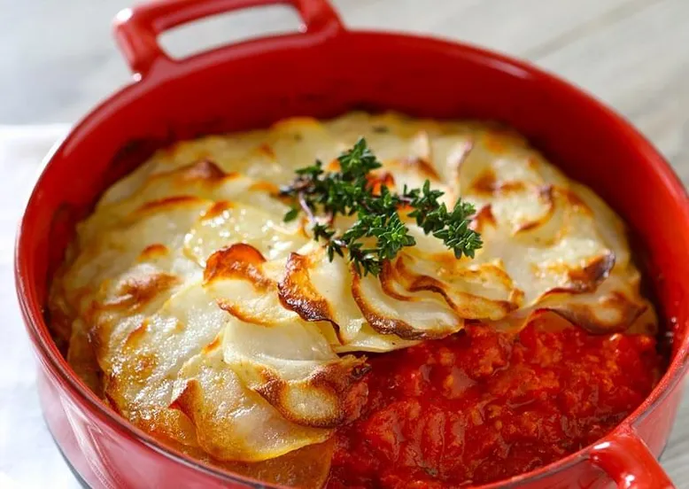 Cocotte rouge de gratin dauphinois sur sauce tomate, garni de thym frais.