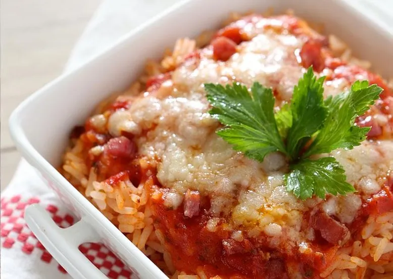 Plat à gratin de riz à la sauce tomate, lardons et fromage fondu, garni de persil.