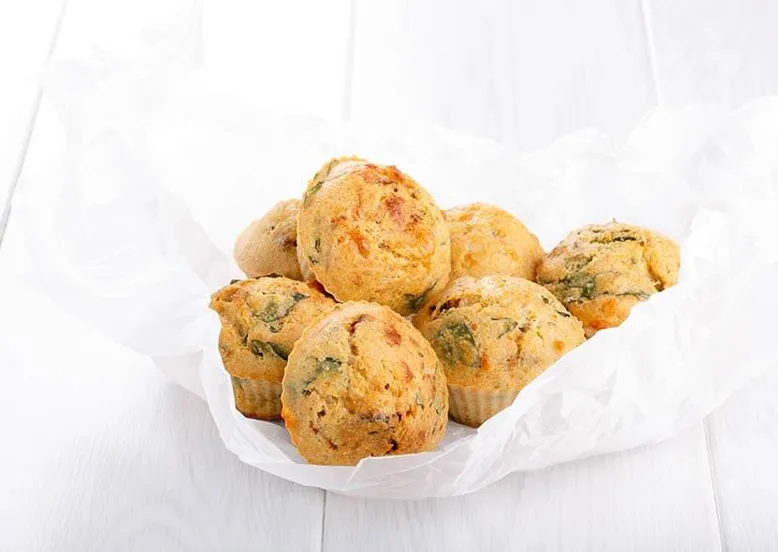 Pile de muffins salés au fromage et herbes, enveloppés dans du papier sulfurisé blanc.