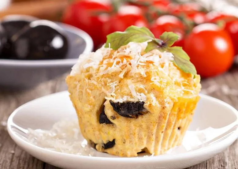 Muffin salé aux olives, parmesan et basilic, sur une petite assiette blanche.