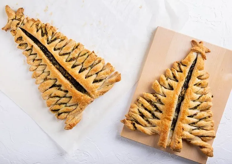 Deux sapins de Noël en pâte feuilletée garnis de pesto, sur papier cuisson.