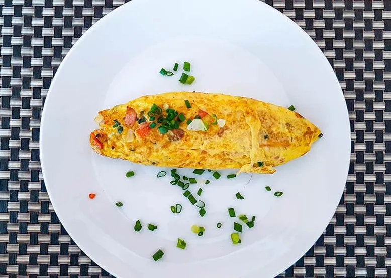 Omelette nature garnie de ciboulette ciselée sur une assiette blanche.