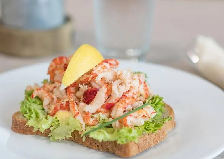 Tartine de pain grillé à l'avocat et crevettes nordiques, garnie de citron.