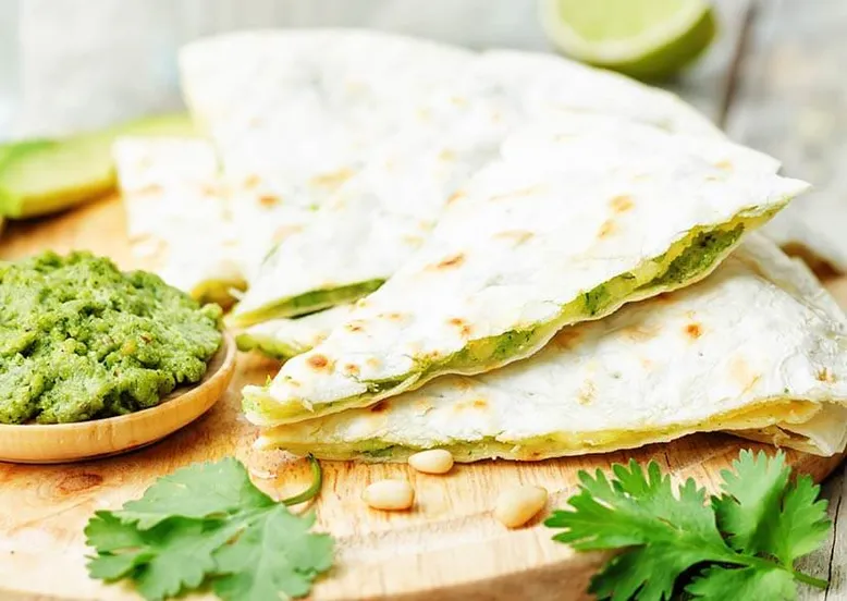 Quesadillas garnies de pesto, servies avec un bol de pesto, pignons de pin et coriandre.