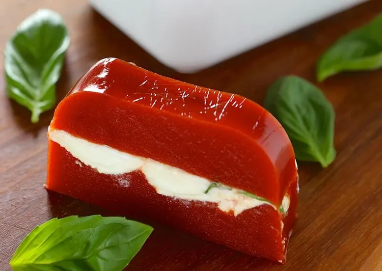 Terrine de gelée de tomate et mozzarella, garnie de feuilles de basilic frais.