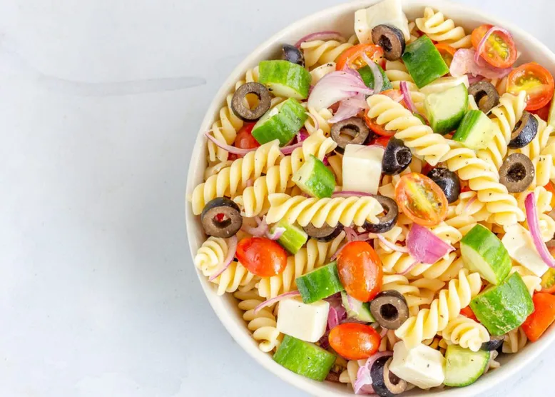 Saladier de salade de fusilli aux concombres, tomates cerises, oignons rouges, olives noires et feta.