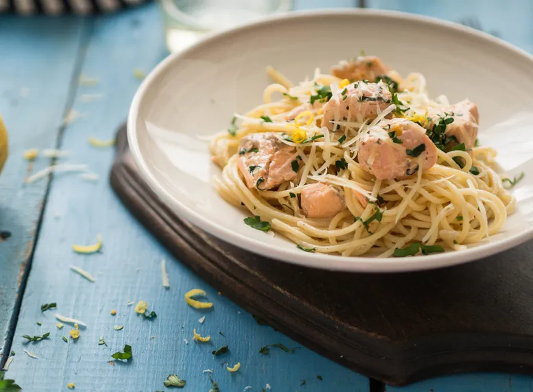 Assiette de spaghetti au saumon, parmesan, zeste de citron et persil sur une table en bois bleu.