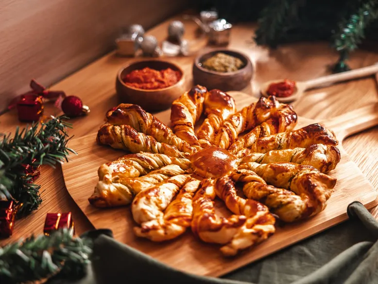 Tresse feuilletée en forme d'étoile garnie de pesto, décorée pour Noël, avec sauces.