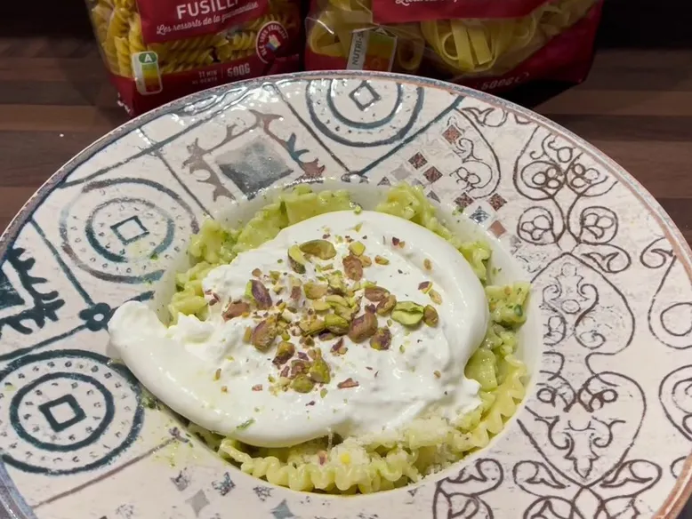 Gros plan sur des mafaldine vertes à la burrata crémeuse et pistaches concassées.