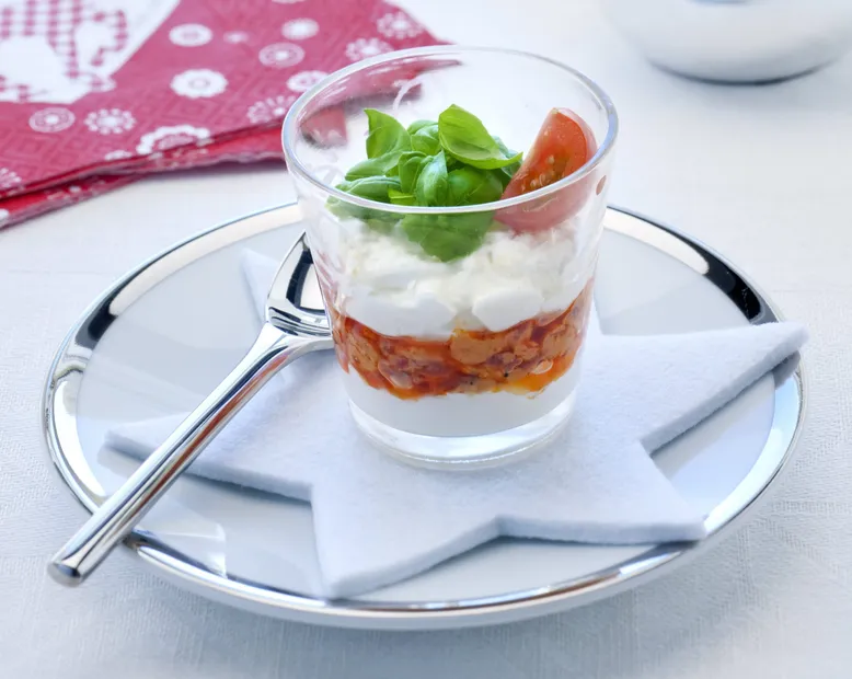 Verrine apéritive avec couches de sauce tomate, fromage frais, basilic et tomate cerise.