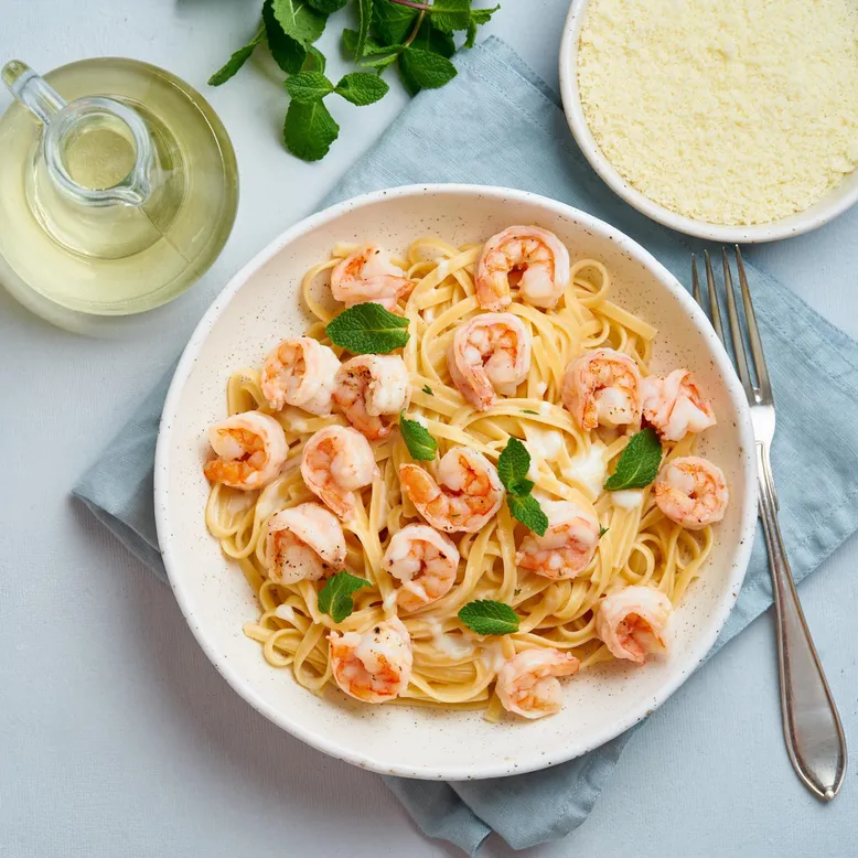 Bol de tagliatelles aux crevettes dans une sauce crémeuse, garni de feuilles de menthe.